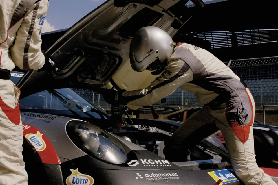The Community of Speed: mechanik w kasku nad otwartą klapą Porsche